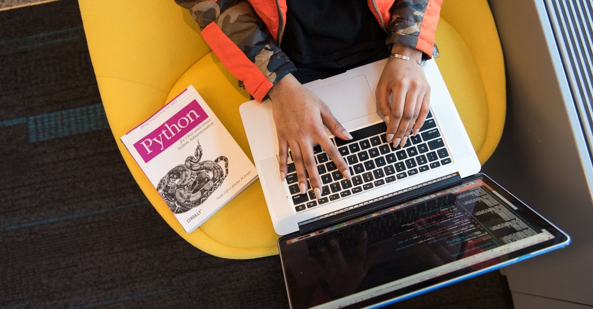 A developer typing code on a laptop with a Python book beside in an office.