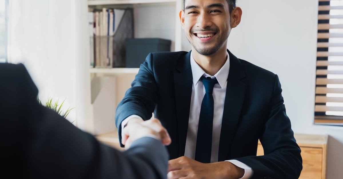 Confident businessman in suit shaking hands at office desk, symbolizing successful partnership.