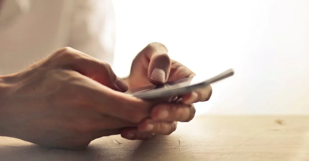 Close-up of an individual's hands holding a smartphone on a table indoors.