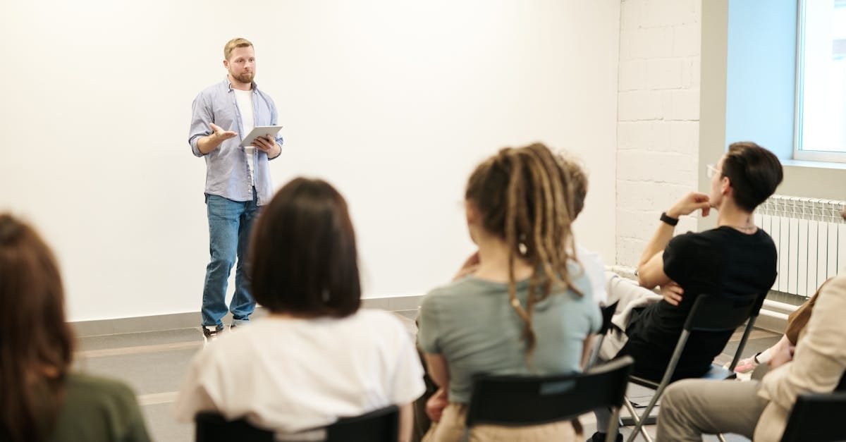 Man presenting with tablet to a small seated audience in a modern indoor setting.