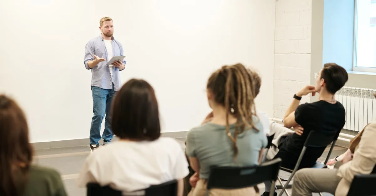 Man presenting with tablet to a small seated audience in a modern indoor setting.