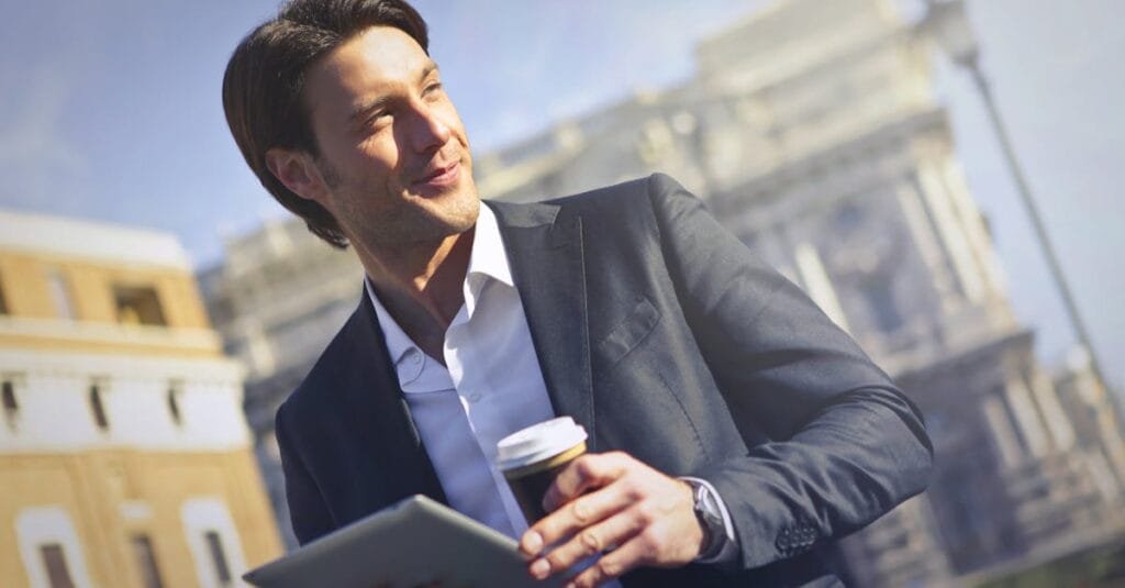 Confident businessman with tablet and coffee outdoors.
