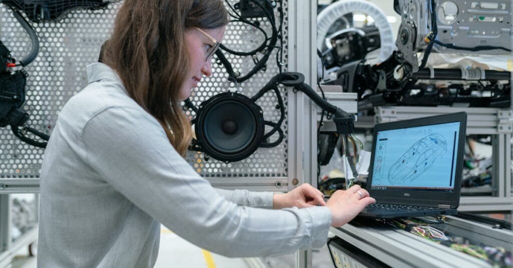 Woman conducting engineering research in a sound system workshop using a laptop.