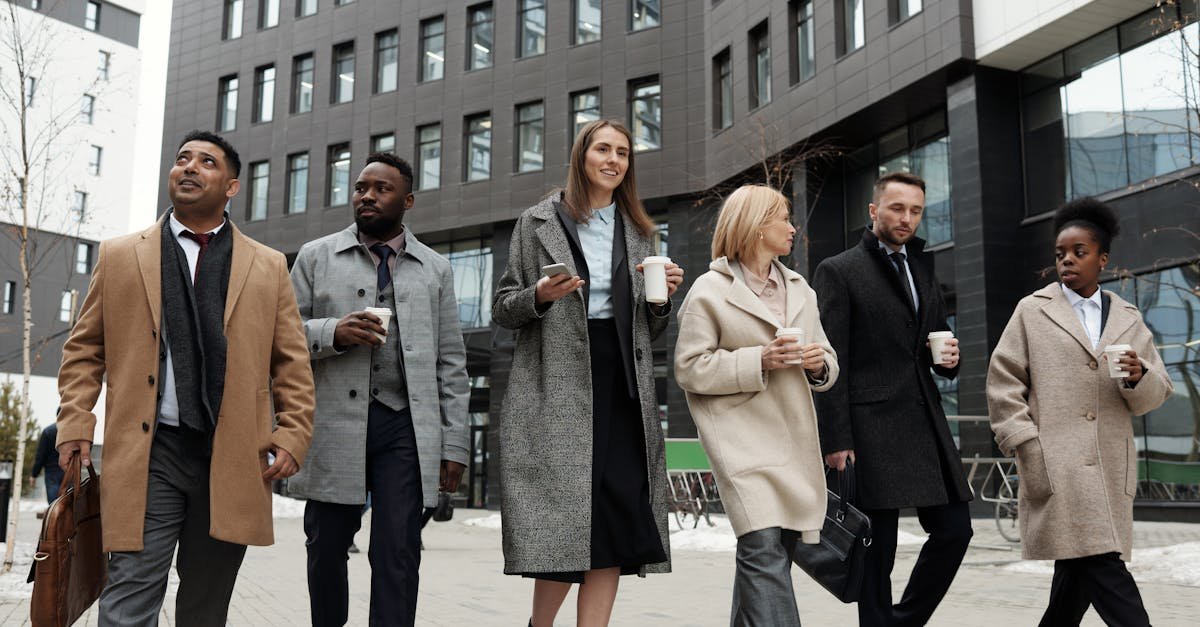 A diverse group of business professionals walking outdoors with coffee cups, showcasing teamwork.