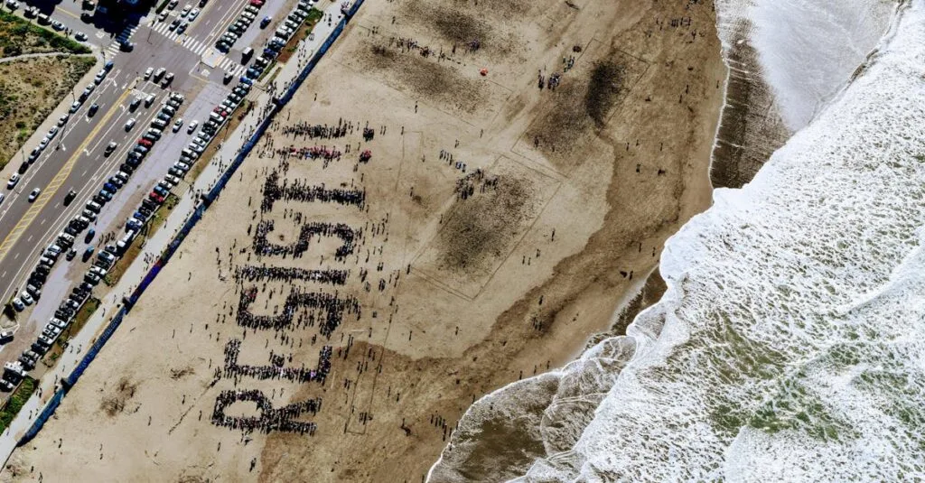 A large group on a beach forms the word "Resist" in powerful demonstration.