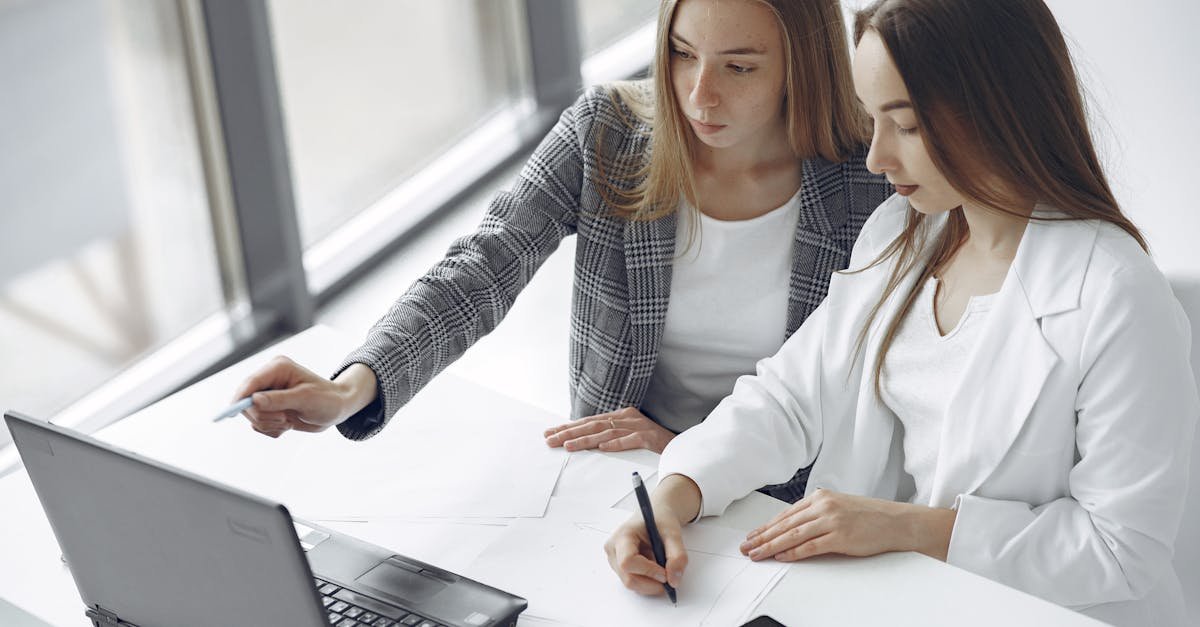 Two professional women collaborating on a project with a laptop and documents.