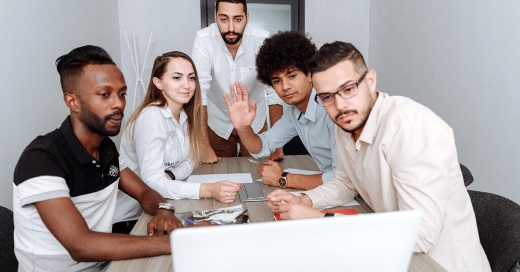 Diverse team collaborating around a laptop in a modern office. Multi-ethnic group engaged in a team meeting.