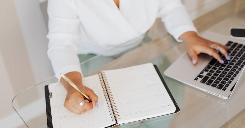 A person planning and typing on a laptop at a glass desk.