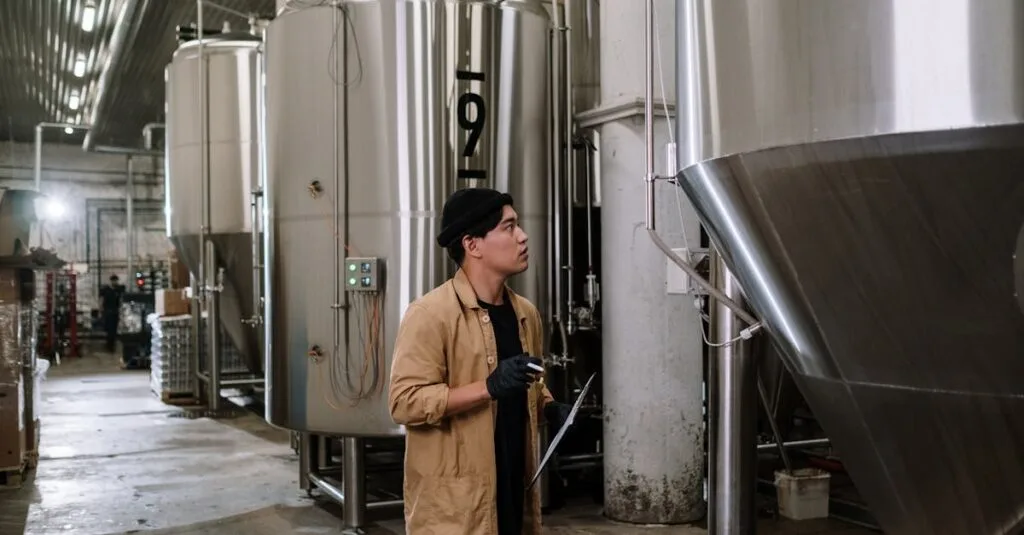 Asian man inspecting stainless steel tanks in a brewery, showcasing modern industrial processes.