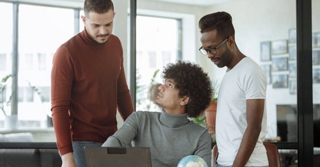 Three colleagues discussing a project with a laptop and a globe in a modern office setting.
