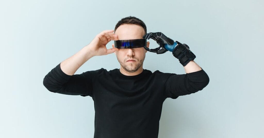 Adult man adjusts futuristic sunglasses with prosthetic arm against neutral background.