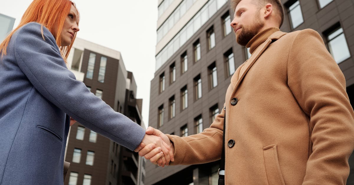 Man and woman shaking hands in a cityscape setting, symbolizing a business partnership.