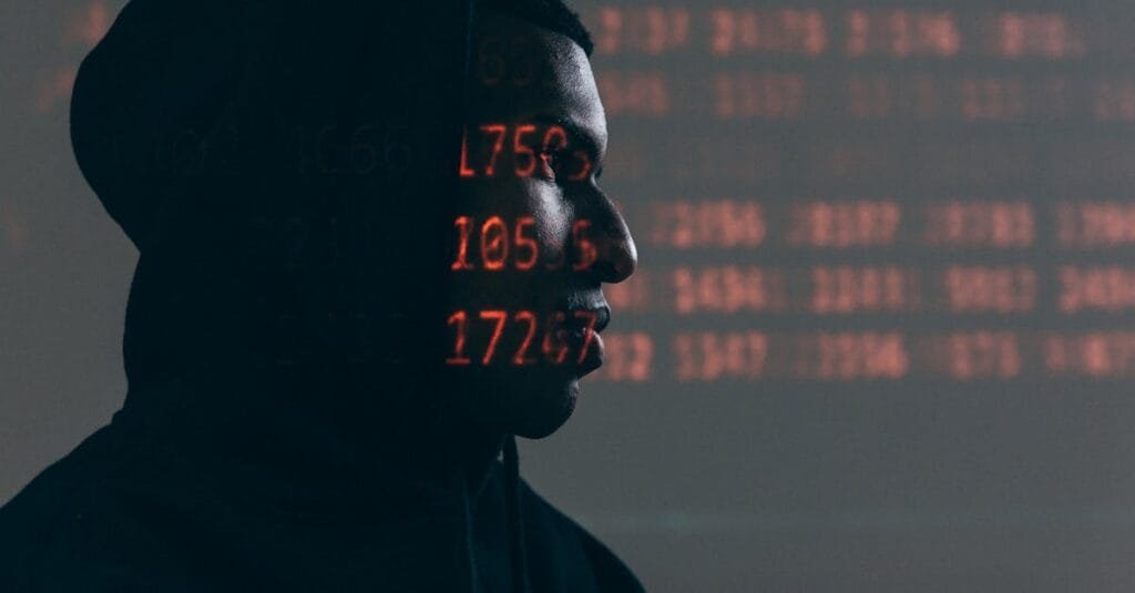 Side profile of a man in a hoodie, surrounded by red code, depicting cybersecurity theme.