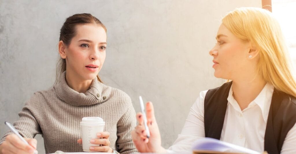 Two women engaging in a professional conversation over coffee and notes.