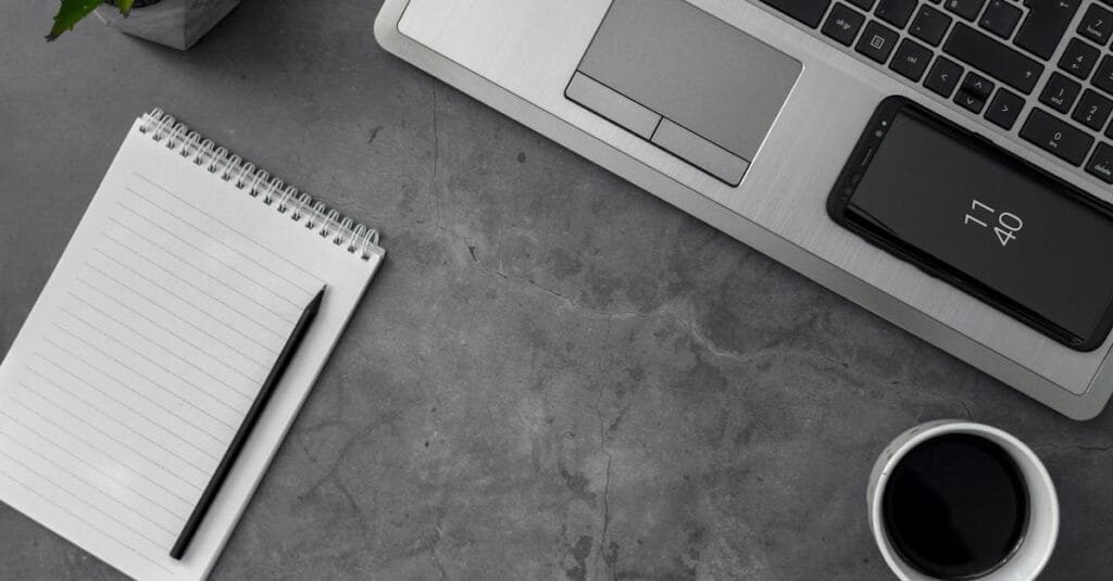 Minimalist workspace featuring laptop, smartphone, notepad, pencil, and coffee cup for productivity.