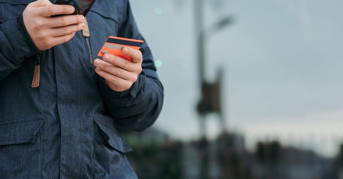 A person outdoors using a smartphone and credit card, illustrating online payments.