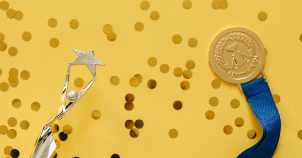 Golden medal and silver trophy with confetti on yellow surface, celebrating achievement.