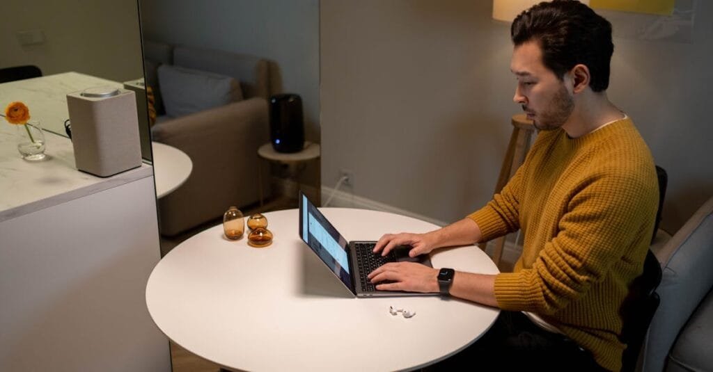 A man in a yellow sweater works on a laptop at home, creating a cozy and modern atmosphere.