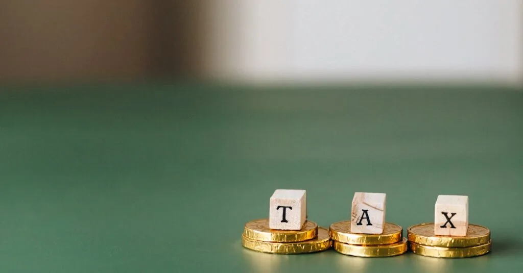 Stacked gold coins with wooden blocks spelling 'TAX' on a green backdrop.