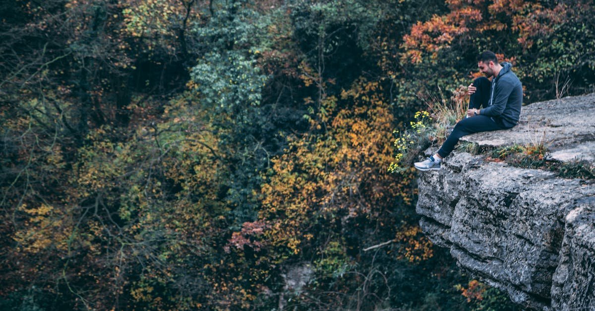 A man sits pensively on a cliff edge surrounded by autumn foliage.