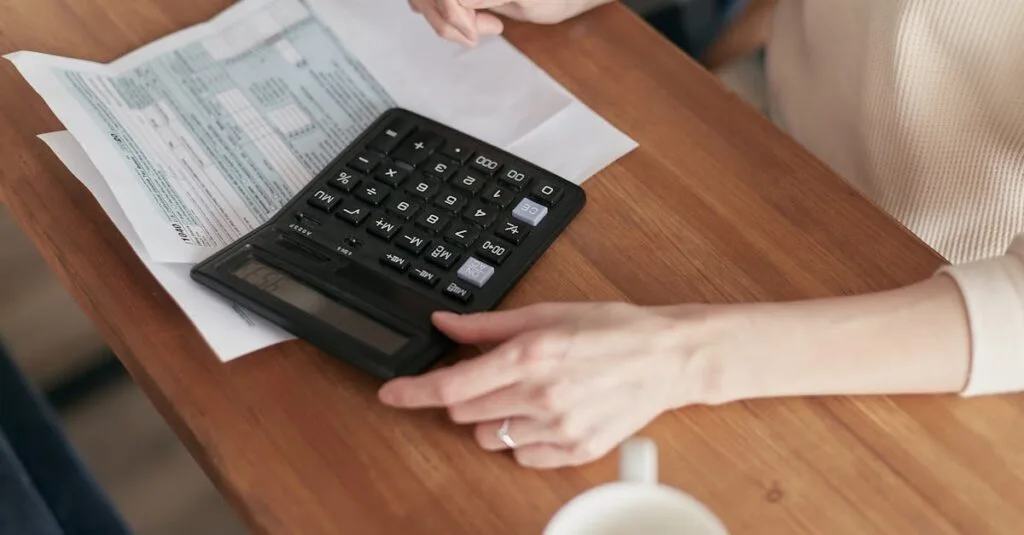 Focused individual using calculator to manage personal finances at wooden desk.