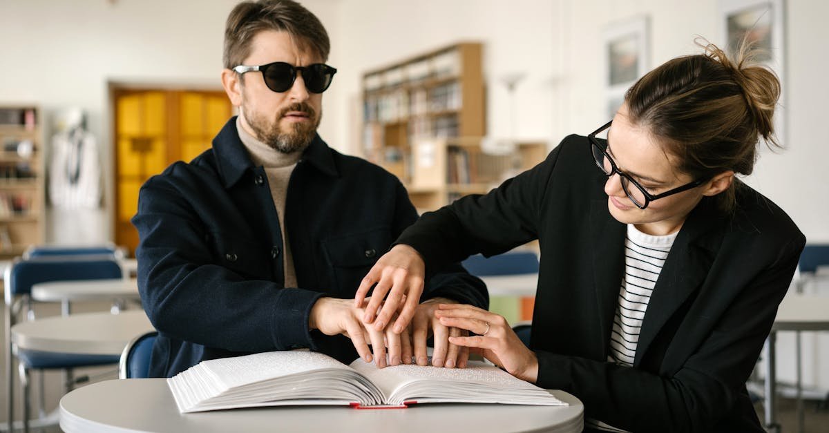 Man reading Braille with caregiver assistance in a library setting, highlighting accessibility and support.