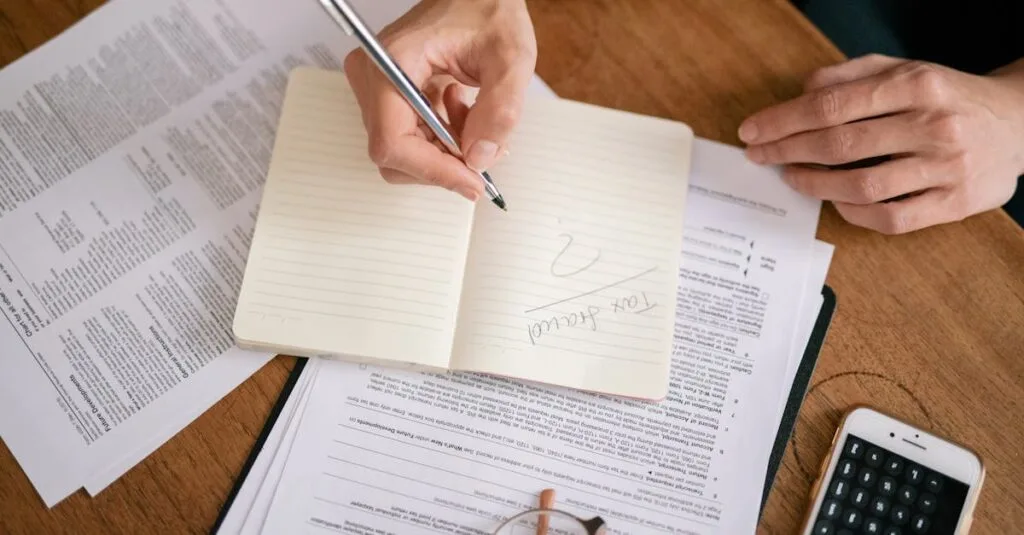 Close-up of hands writing on a notebook surrounded by tax documents and a smartphone.