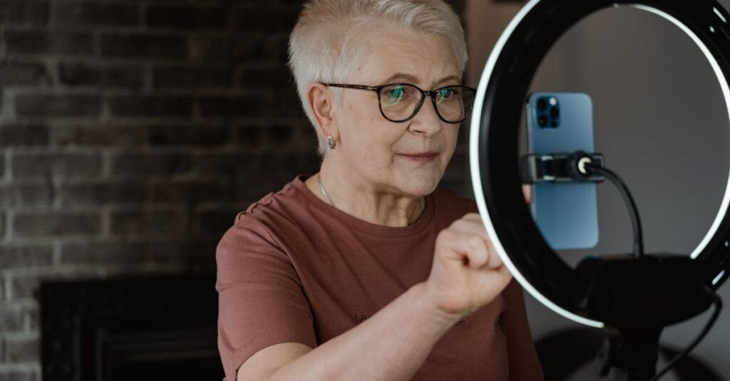 Elderly woman engaging with technology using a smartphone and ring light indoors.