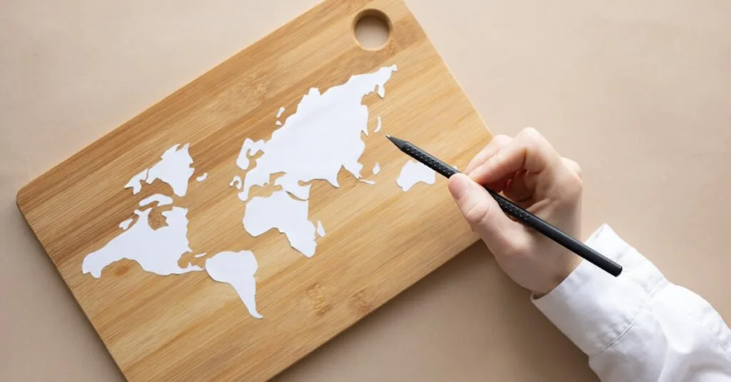 Hand crafting a world map on a bamboo cutting board using a pencil on beige background.