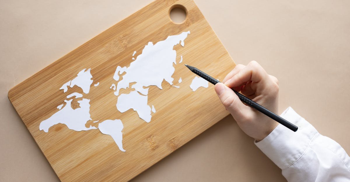 Hand crafting a world map on a bamboo cutting board using a pencil on beige background.