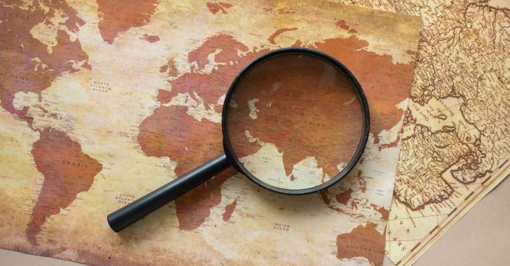A top view of a vintage world map with a magnifying glass highlighting regions for exploration.