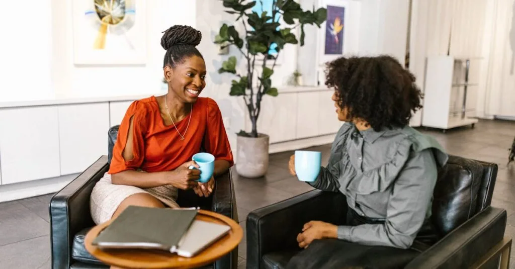 Two businesswomen enjoy a coffee break and conversation in a modern office setting.