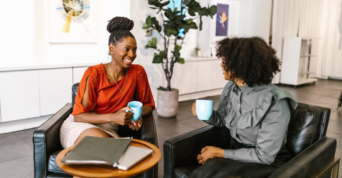 Two businesswomen enjoy a coffee break and conversation in a modern office setting.