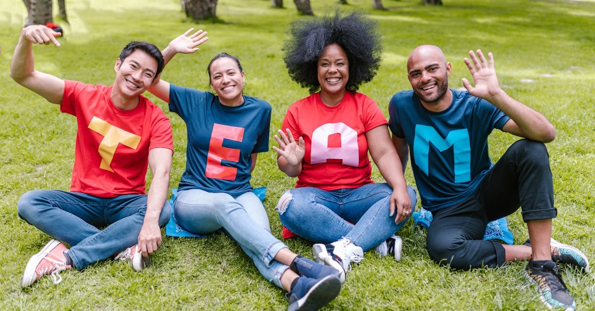 Multiracial team sitting on grass in park, wearing 'TEAM' shirts, showing unity.