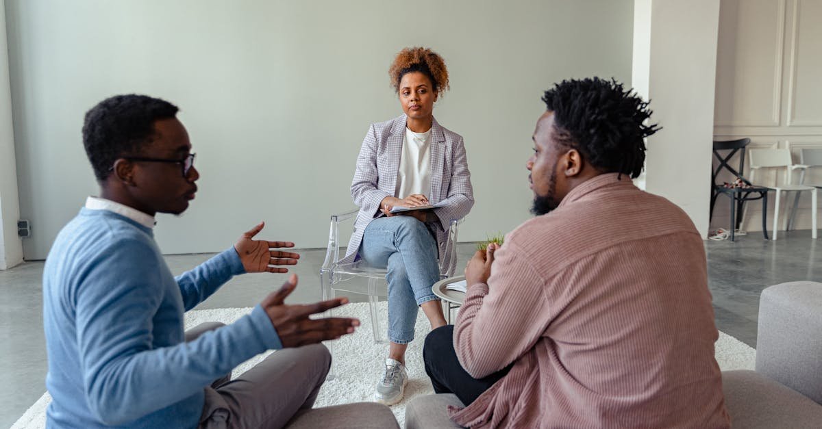 A therapist mediates a session with two men on a couch discussing mental health.