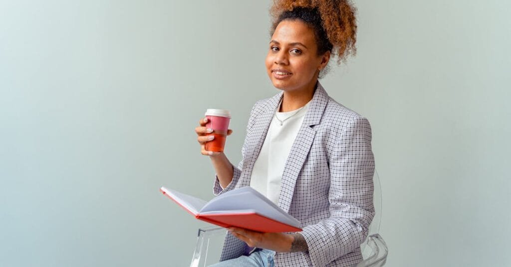 Smiling professional woman holding a coffee and notebook in a light office setting, exuding confidence and knowledge.