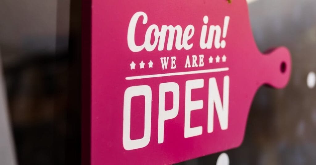 A bright pink "Come in! We are Open" sign hanging in a store window welcoming customers.