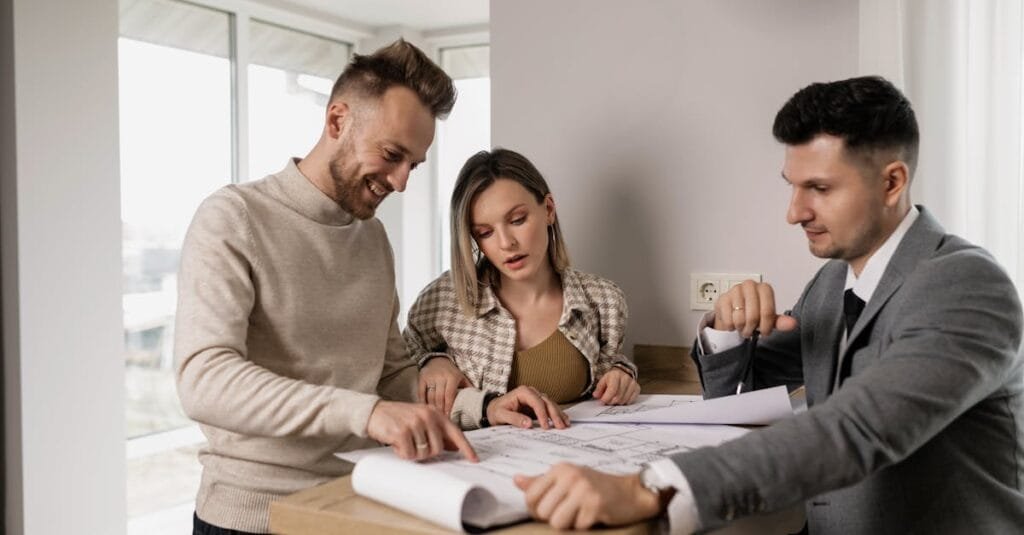 Three adults reviewing real estate blueprints indoors at a table.