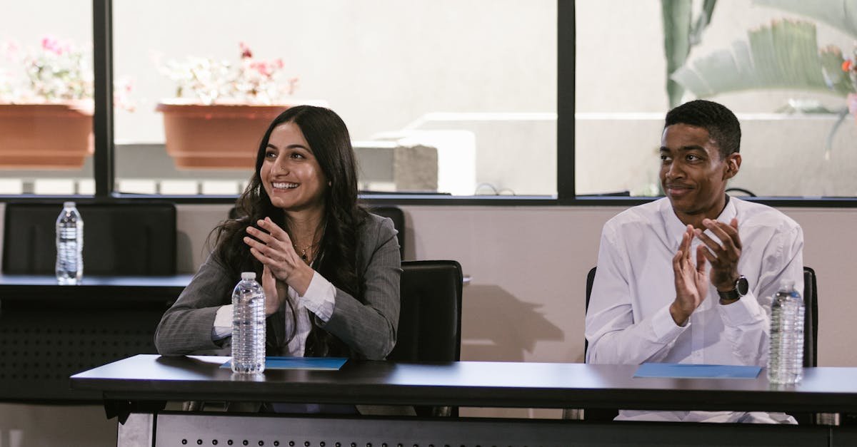 Smiling coworkers clapping at a table in a professional setting indoors.