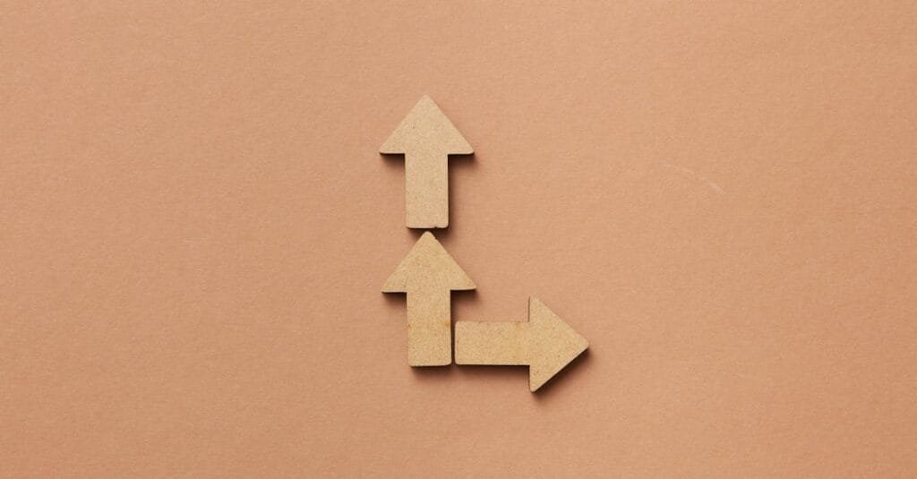 Three cardboard arrows arranged on a brown background, symbolizing direction and choice.