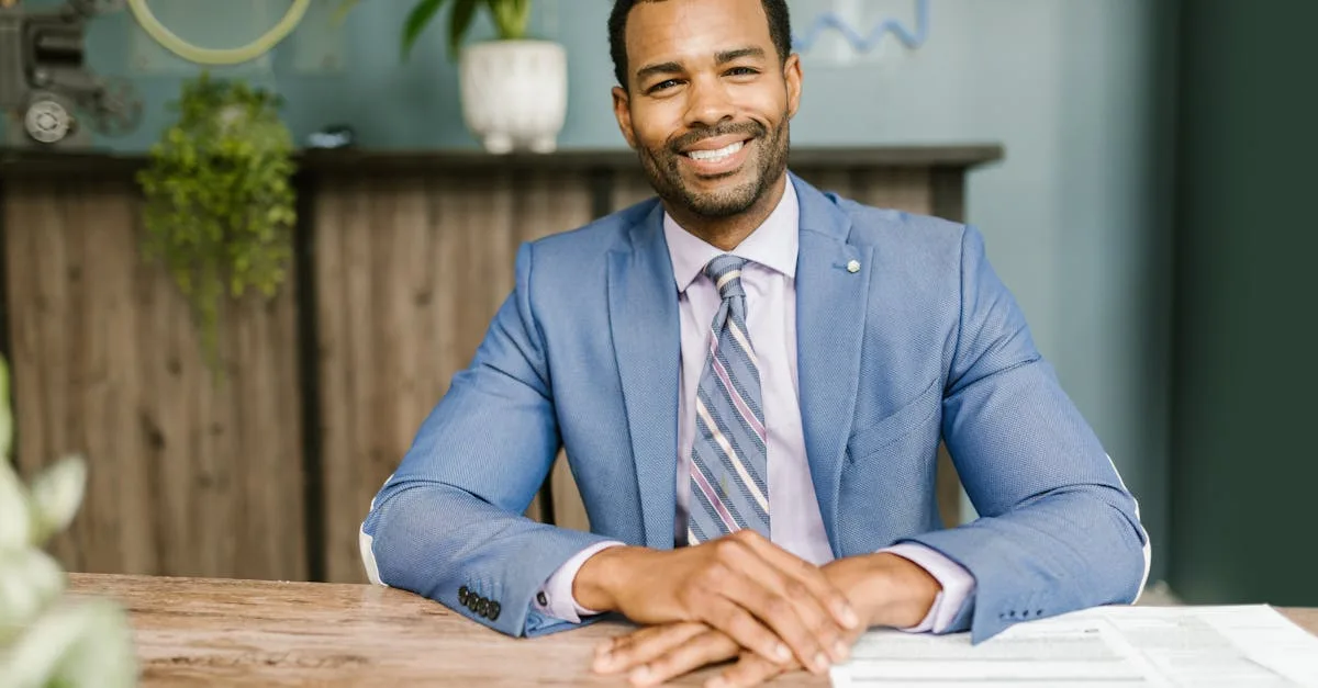 Smiling businessman in office attire sitting at a desk with documents.