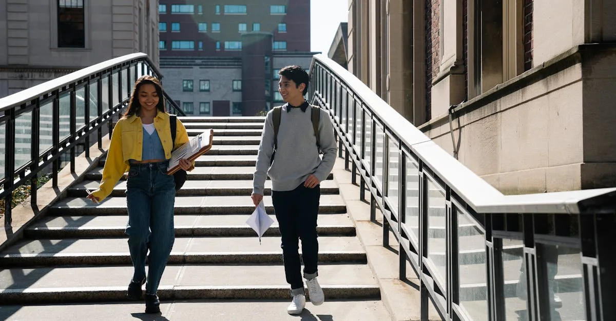 Two university students walking down a staircase, carrying documents and smiling during the day.