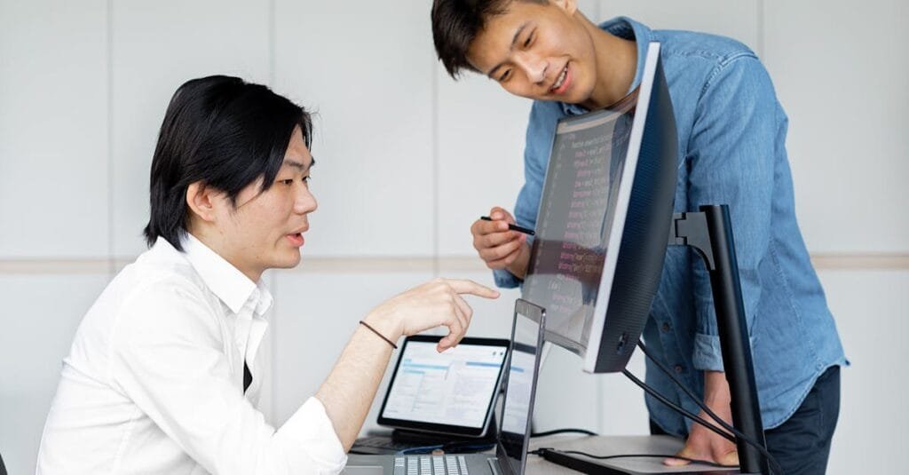 Two Asian men collaborating on a project using computers in an office.