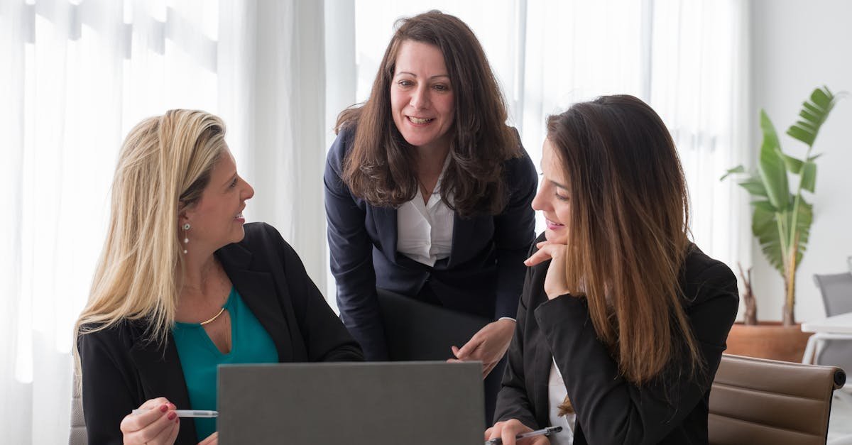 Three professional women engaged in a collaborative business discussion in a modern office setting.