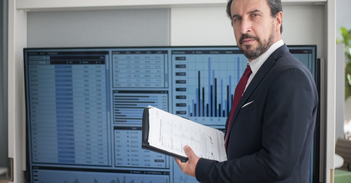 Businessman in a suit holds documents analyzing graphs on a screen, reflecting data analysis.