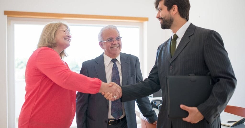 Senior couple meeting with a real estate agent indoors, shaking hands to finalize a home agreement.