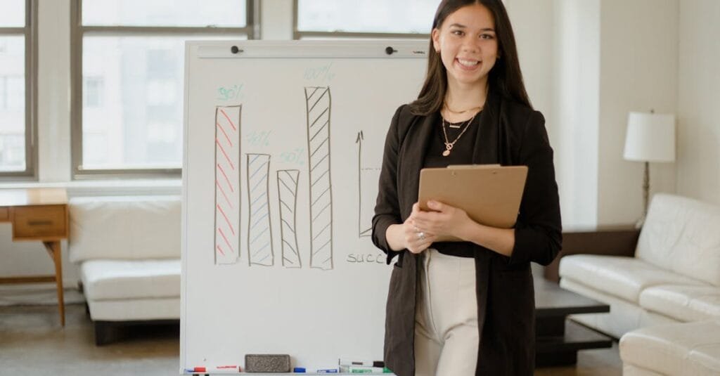 Confident businesswoman presenting charts and data analysis on a whiteboard in a modern office setting.