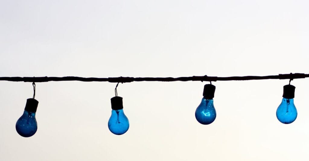 Minimalist image of blue light bulbs hanging on a wire against a neutral sky background, offering creative copyspace.