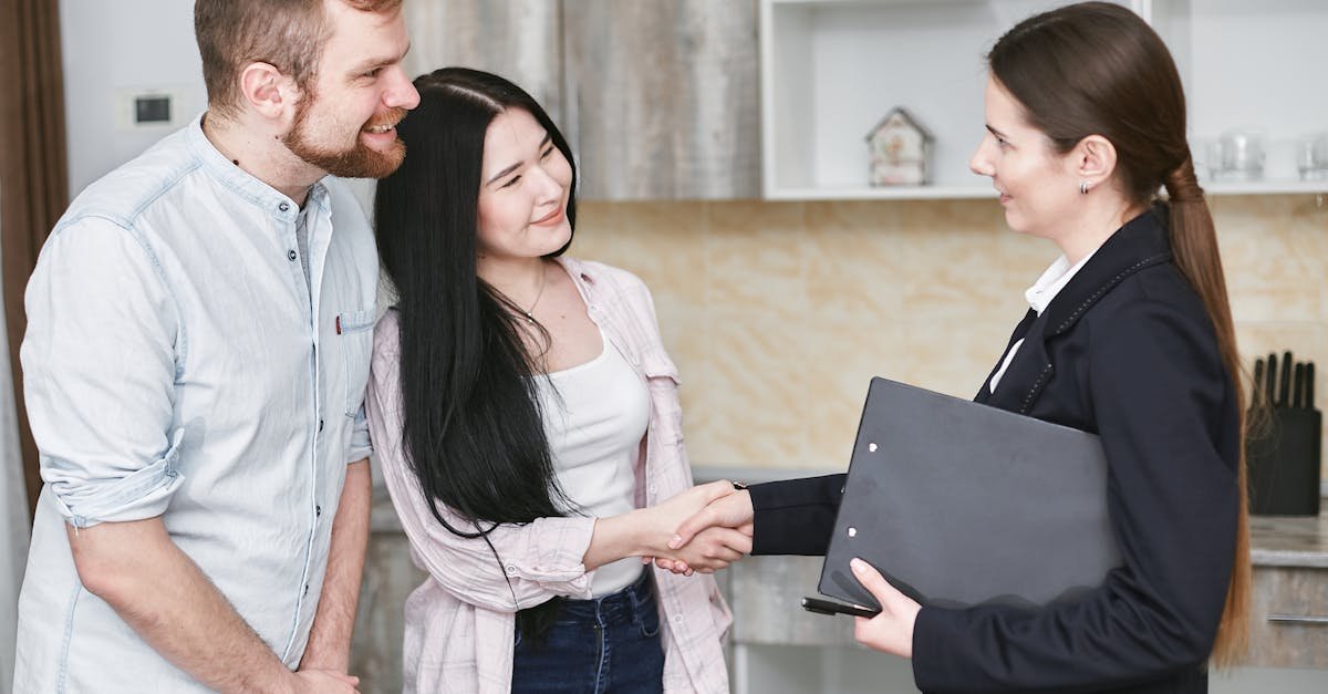 A real estate agent greets a couple with a handshake in a modern home interior.