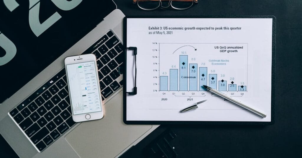 Top view of a financial data analysis setup with laptop, smartphone, and graph on clipboard.